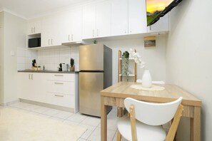 A modern kitchen with white cabinets, a stainless steel refrigerator, and a dining table with a white vase. - Snowy Love - CBD, Parking & Cozy (Darwin City)