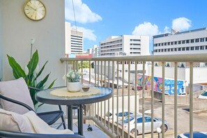 A balcony with a round table, a clock, and a view of city buildings and parked cars. - Snowy Love - CBD, Parking & Cozy (Darwin City)