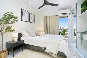 A bedroom with a bed, bedside table, lamp, and a potted plant. - Snowy Love - CBD, Parking & Cozy (Darwin City)
