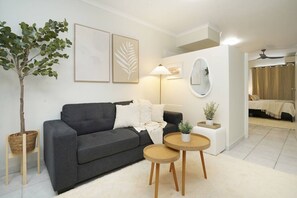 A modern living room with a grey sofa, a small round table, a floor lamp, and a potted plant. - Snowy Love - CBD, Parking & Cozy (Darwin City)