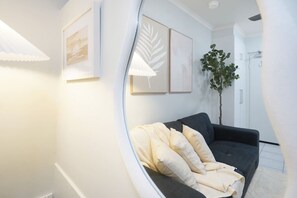 A modern living room with a dark grey sofa, white cushions, and a large plant. - Snowy Love - CBD, Parking & Cozy (Darwin City)