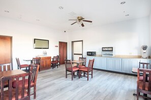 A dining area with wooden chairs and tables, a kitchen with light blue cabinets, a ceiling fan, and a microwave.