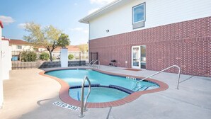 A swimming pool with a brick wall and a white building in the background. - Townhouse Clute Lake Jackson|King Bed (Clute TX)