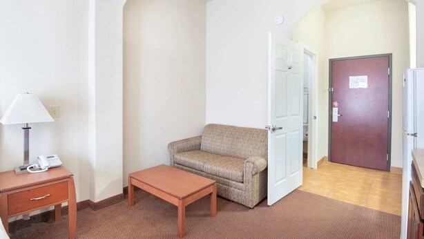 A hotel room with a sofa, a small table, a lamp, a telephone, and a door leading to another room. - Townhouse Clute Lake Jackson|King Bed (Clute TX)