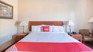 A hotel room with a bed, two bedside tables, a chair, and a painting on the wall. - Townhouse Clute Lake Jackson|King Bed (Clute TX)