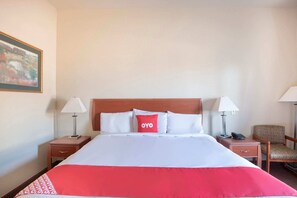 Ein Hotelzimmer mit einem Bett, zwei Nachttischen, einem Sessel und einem Bild an der Wand.