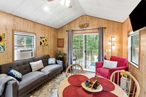 A cozy room with a sofa, a red chair, a dining table with a tray, and a large window.