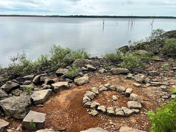 A natural landscape with a body of water, rocky terrain, and sparse vegetation.