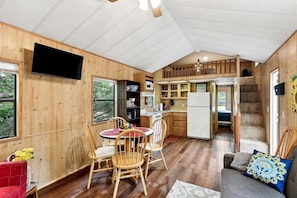 A wooden interior with a dining area, kitchen, and a staircase leading to an upper level.