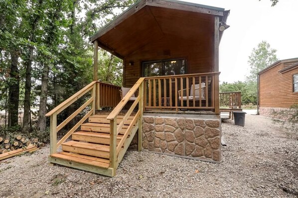 A cabin with a wooden staircase leading to a porch, a stone foundation, and a view of the surrounding forest.