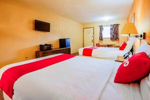 Quarto de hotel com duas camas, televisão, escrivaninha com computador, luminária e janela com cortinas.