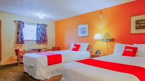 Une chambre d’hôtel avec deux lits, un bureau, une chaise, une fenêtre avec des rideaux, une lampe et un tableau encadré au mur.