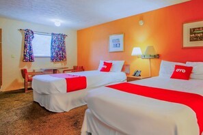 Hotellihuone, jossa on kaksi sänkyä, työpöytä, tuoli, ikkuna verhoilla, lamppu ja seinällä oleva kehystetty kuva.