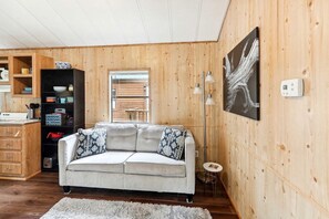 Ein gemütliches Wohnzimmer mit einer Couch, einem Couchtisch, einem Bücherregal, einem Fenster und einem Bild an der Wand.
