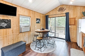 Un intérieur en bois avec une table ronde, des tabourets de bar, un banc, un téléviseur et une vue sur l’extérieur.