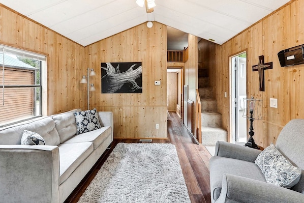 L’intérieur d’une cabane en rondins, avec un canapé, un fauteuil et un escalier menant à une mezzanine.
