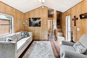 Ein Holzblockhaus-Innenraum mit einer Couch, einem Sessel und einer Treppe, die zu einem Erker führt.