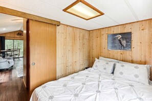 Ein schlafreicher Raum mit Holzwänden, einem Bett, einem Vogelgemälde und Blick auf eine Terrasse.