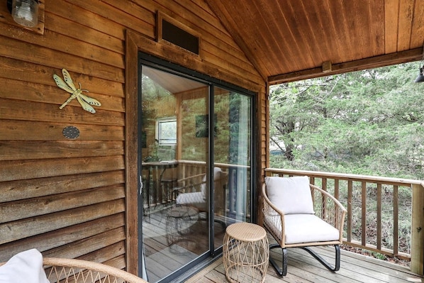 A wooden deck with a glass door leading to a room, wicker chairs, and a small round table.