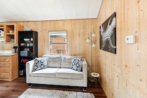 A cozy living room with a sofa, a coffee table, a bookshelf, a window, and a painting on the wall. - Idyllic Rental Cabin for Romantic Getaways and Outdoor Adventures by Toronto Lake, Kansas (Toronto)