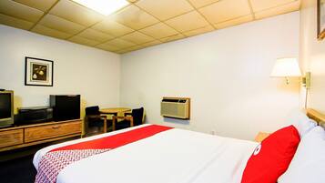 A hotel room with a bed, a desk, a chair, a television, and a wall-mounted air conditioner.