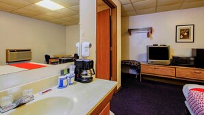 A hotel room with a bathroom, a bed, a TV, a microwave, a coffee maker, and a mirror.