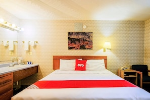 Une chambre d’hôtel comprenant un lit, une table de chevet, une lampe, un miroir et un meuble-lavabo dans la salle de bain.