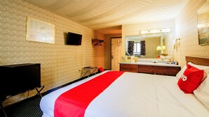 A hotel room with a bed, a TV, a desk, a mirror, and a bathroom.