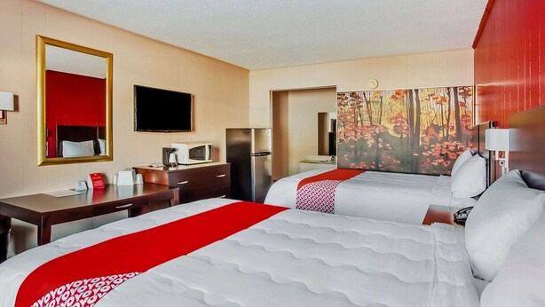 A hotel room with two beds, a desk, a TV, a microwave, and a refrigerator.