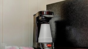 A coffee maker with a cup holder, a red button, and packets on the table.