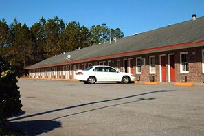 A motel with a row of rooms, a parking lot, and a white car parked in front. - Queen Bed | Non-Smoking (Ridgeland SC)