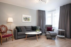 Ein modernes Wohnzimmer mit einem grauen Sofa, einem runden Couchtisch, einem Holzstuhl, einem kleinen Beistelltisch und einer Lampe.
