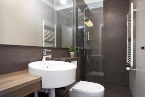 Ein modernes Badezimmer mit rundem Waschbecken, Toilette und einer Duschkabine aus Glas.