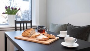 Pöydällä on leipää, muki ja kuppeja, ikkunasta avautuu näkymä ja siellä on myös kasvi.