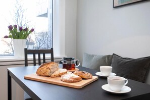 Ein Tisch mit Brot, einer Tasse und einigen Tassen, ein Fenster mit Aussicht und eine Pflanze.