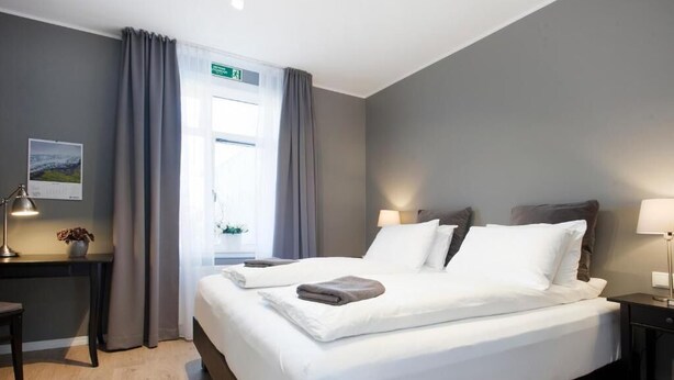 Hotellihuone, jossa on sänky, yöpöydät, työpöytä ja ikkuna, jossa on verhot.