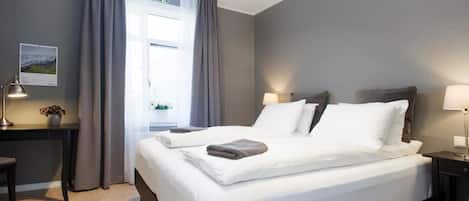 Una habitación de hotel con cama, mesitas de noche, escritorio y ventana con cortinas.