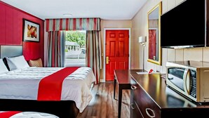 A hotel room with a bed, a TV, a microwave, a desk, and a red door.