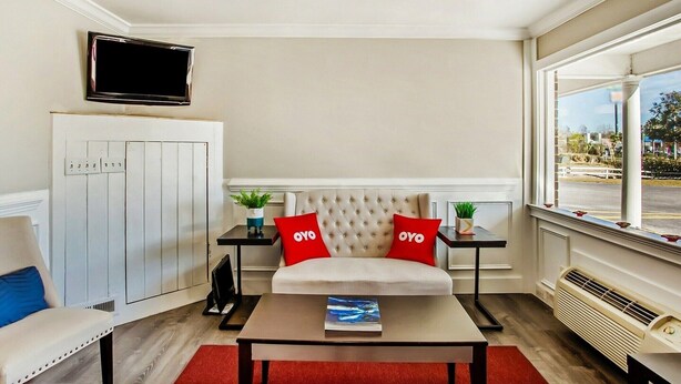 A modern hotel room with a sofa, a flat-screen TV, a table with a book, and a window with a view.