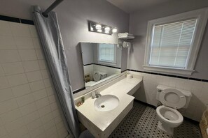 Een badkamer met een witte wastafel, een spiegel, een toilet en een raam met zonwering.