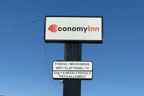 A signboard for Economy Inn with amenities like a fridge, microwave, WiFi, flat panel TV, and daily & weekly rentals.