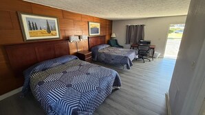 A hotel room with two beds, wooden headboard, framed artwork, a desk, chair, and a window with curtains.