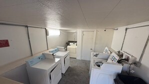 Un lavadero con lavadoras y secadoras, un letrero que indica que es lavadero, y una puerta que da a otra habitación.