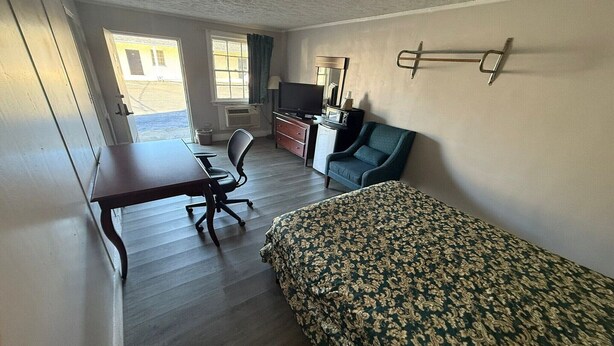 Una habitación con cama, escritorio, silla, televisor y ventana.