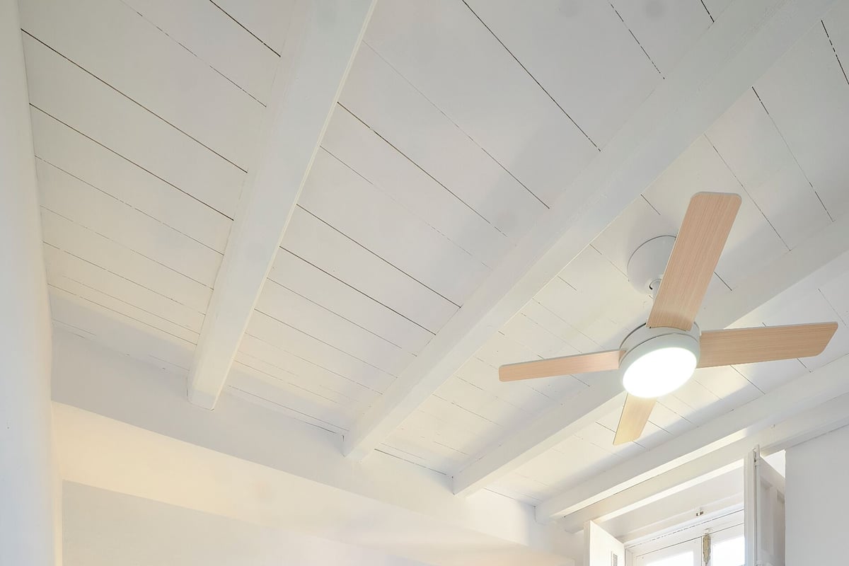 A bedroom with a bed, ceiling fan, bedside lamps, and a door with a balcony view.