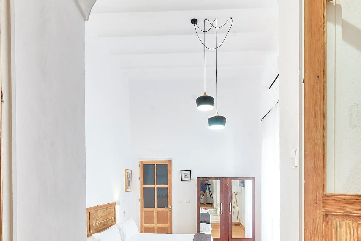 A bedroom with a bed, wooden floor, white walls, a wooden door, and a mirror.