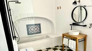 Ein Badezimmer mit Schachbrettboden, einer Badewanne, einer Toilette, einem Waschbecken mit Spiegel und einem Ablagebereich für Toilettenartikel.