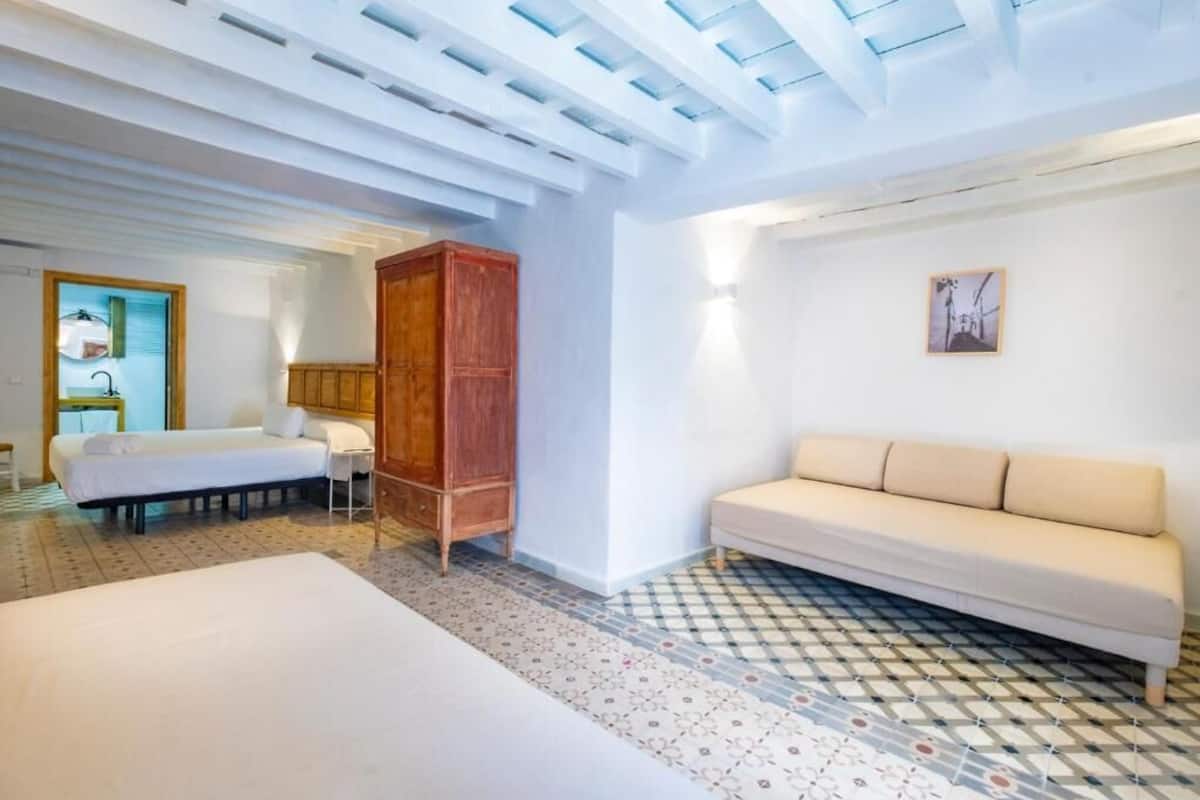 A hotel room with a bed, a sofa, a wooden cabinet, a tiled floor, and a skylight.