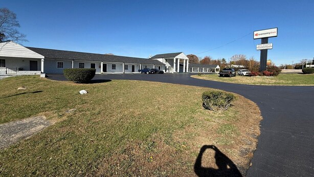 A motel with a large sign, a covered parking area, and a grassy lawn.