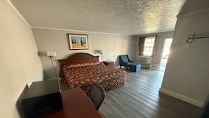 A hotel room with a bed, a desk, a chair, a painting on the wall, and a view of the outdoors.